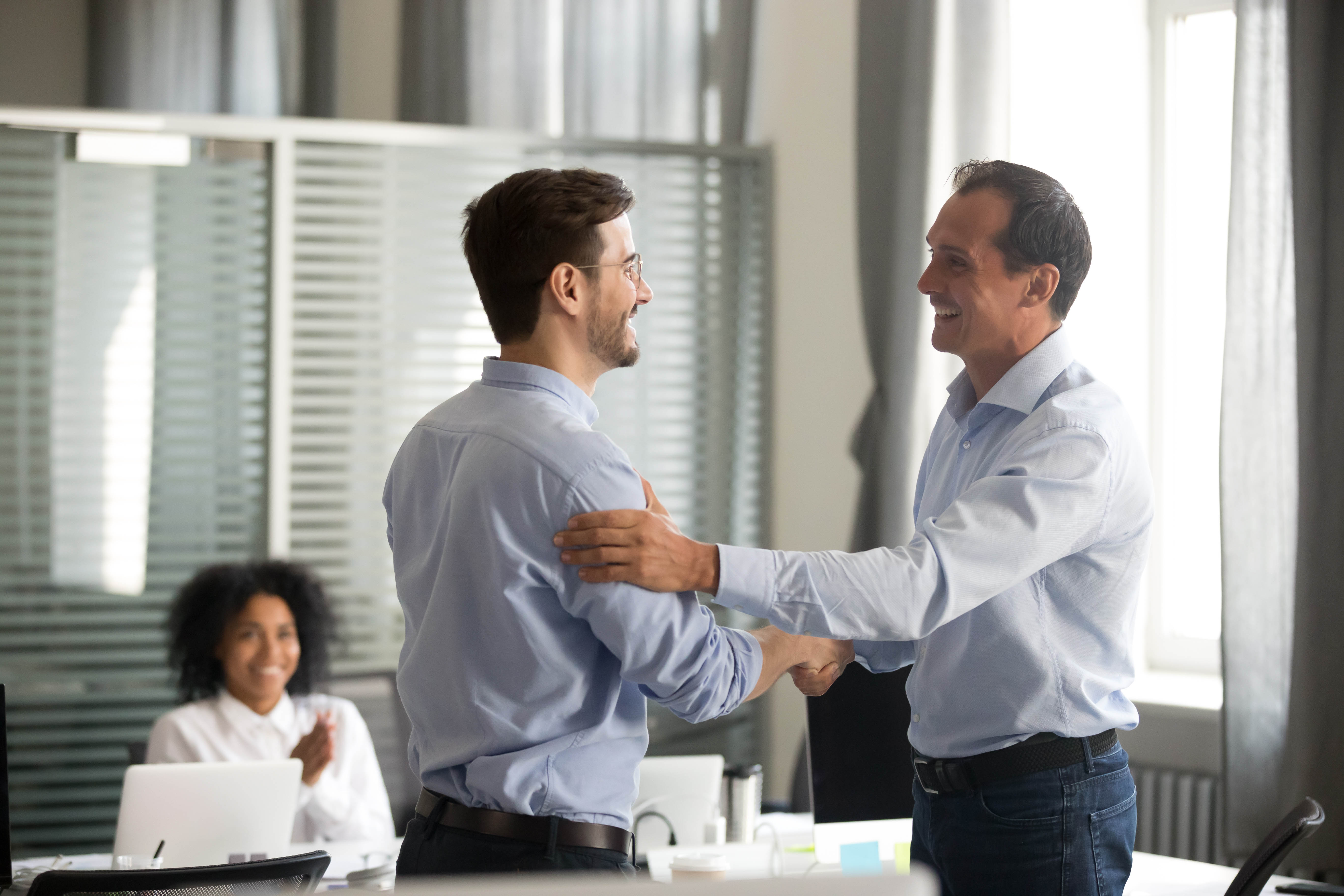 Male boss showing support and appreciation for his male colleague with a hand on his back and handshake in a meeting room